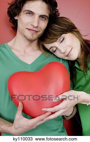 Couple holding plastic heart, woman resting her head on man's shoulder View Large Photo Image Stock Image - Couple holding plastic heart, woman resting her head on man's shoulder. Fotosearch