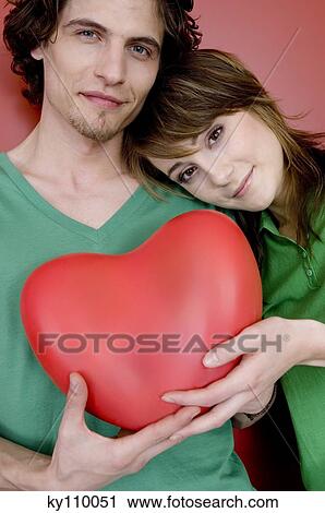 Couple holding plastic heart, woman resting her head on man's shoulder View Large Photo Image Stock Image - Couple holding plastic heart, woman resting her head on man's shoulder. Fotosearch