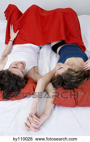 Couple lying in bed, holding hands, elevated view View Large Photo Image Stock Photograph - Couple lying in bed, holding hands, elevated view. Fotosearch