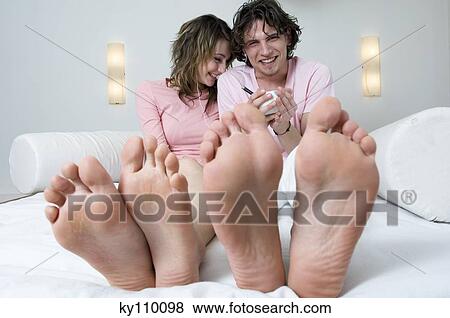 Stock Photo - Couple sitting on a bed, smiling for the camera, barefoot in foreground. Fotosearch