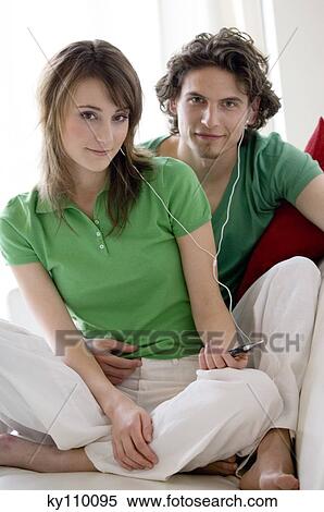 Couple sitting on the floor, listening to MP3 player, looking at the camera View Large Photo Image Stock Photography - Couple sitting on the floor, listening to MP3 player, looking at the camera. Fotosearch