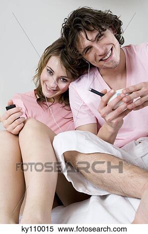 Couple with earphones sitting on a bed, smiling for the camera View Large Photo Image Stock Photography - Couple with earphones sitting on a bed, smiling for the camera. Fotosearch