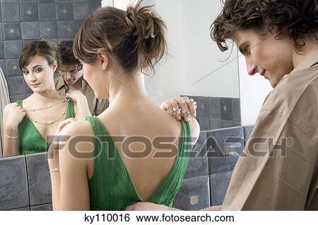 Stock Photograph - Man helping woman get dressed in front of bathroom mirror. Fotosearch