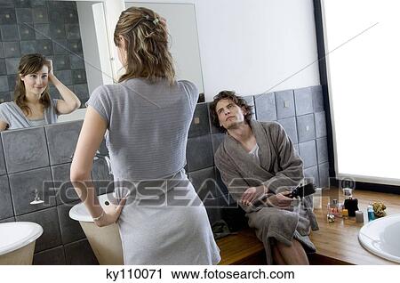 Man in bathrobe sitting, looking at woman standing in front of bathroom mirror View Large Photo Image Stock Image - Man in bathrobe sitting, looking at woman standing in front of bathroom mirror. Fotosearch