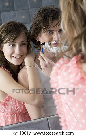 Man shaving in front of bathroom mirror, smiling woman resting on his shoulder View Large Photo Image Stock Photo - Man shaving in front of bathroom mirror, smiling woman resting on his shoulder. Fotosearch