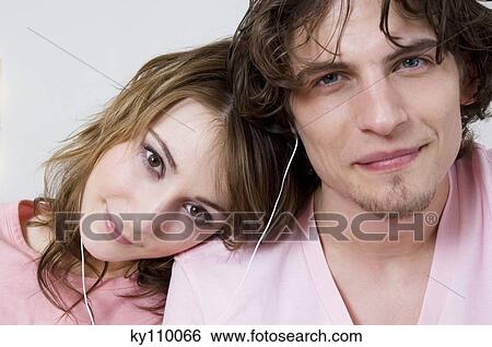 Portrait of a couple wearing earphones, looking at the camera, woman resting her head on man's shoulder View Large Photo Image Stock Photograph - Portrait of a couple wearing earphones, looking at the camera, woman resting her head on man's shoulder. Fotosearch