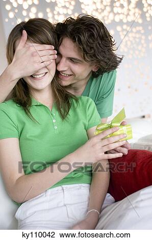 Smiling man giving present to a woman, hands covering her eyes View Large Photo Image Stock Image - Smiling man giving present to a woman, hands covering her eyes. Fotosearch