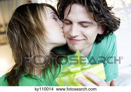 Woman holding a present, kissing man on his cheek View Large Photo Image Picture - Woman holding a present, kissing man on his cheek. Fotosearch