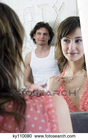 Woman in nightgown trying on necklace in front of bathroom mirror, man in background View Large Photo Image Stock Image - Woman in nightgown trying on necklace in front of bathroom mirror, man in background. Fotosearch