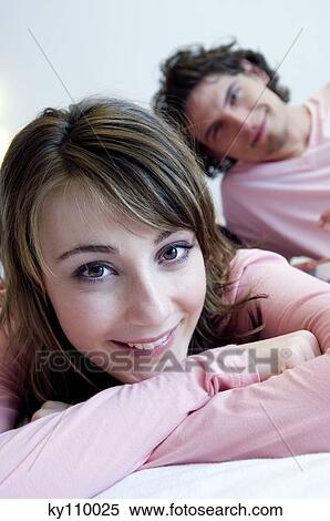 Woman smiling for the camera, man lying on bed in background View Large Photo Image Stock Photography - Woman smiling for the camera, man lying on bed in background. Fotosearch