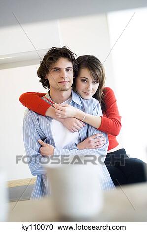Stock Image - Young couple embracing, looking at the camera. Fotosearch