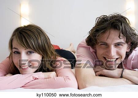 Young couple lying on a bed, smiling for the camera View Large Photo Image Stock Image - Young couple lying on a bed, smiling for the camera. Fotosearch