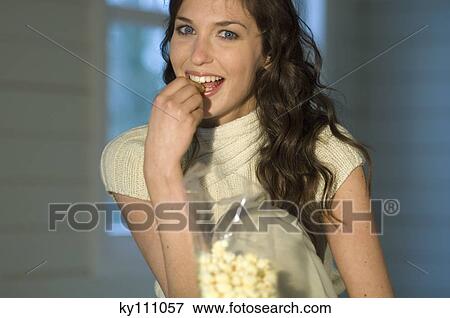 Stock Photo - Portrait of a woman eating popcorn, smiling for the camera. Fotosearch