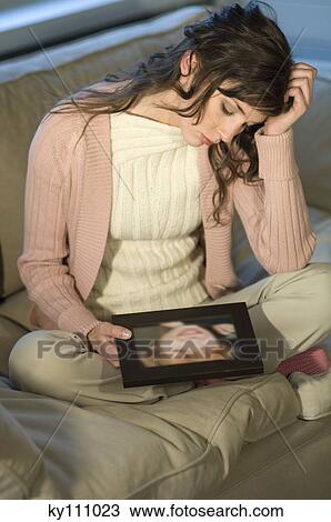 Sad looking woman sitting cross-legged on a sofa looking at child's portrait View Large Photo Image Stock Image - Sad looking woman sitting cross-legged on a sofa looking at child's portrait. Fotosearch