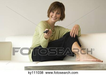 Smiling woman sitting on a sofa using remote-control View Large Photo Image Stock Photo - Smiling woman sitting on a sofa using remote-control. Fotosearch