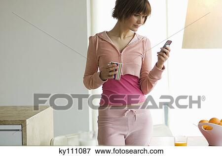 Smiling young woman using mobile phone, holding a cup View Large Photo Image Stock Photo - Smiling young woman using mobile phone, holding a cup. Fotosearch