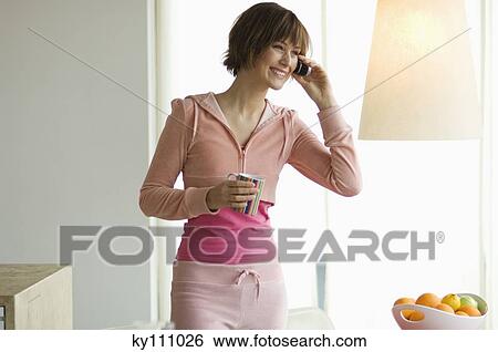 Smiling young woman using mobile phone, holding a cup View Large Photo Image Stock Photograph - Smiling young woman using mobile phone, holding a cup. Fotosearch
