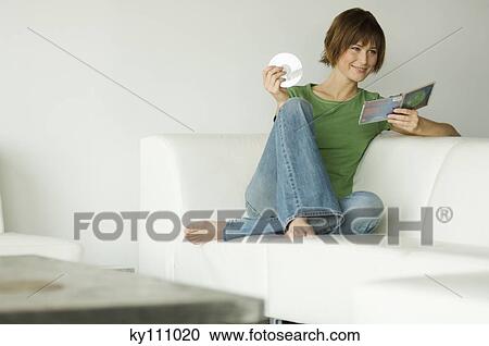 Young smiling woman sitting on a sofa holding CD and its box View Large Photo Image Stock Image - Young smiling woman sitting on a sofa holding CD and its box. Fotosearch