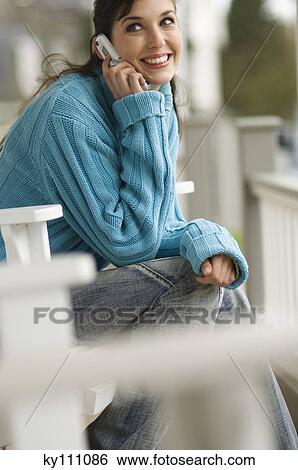 Young smiling woman using mobile phone, sitting on a chair, outdoors View Large Photo Image Stock Photograph - Young smiling woman using mobile phone, sitting on a chair, outdoors. Fotosearch