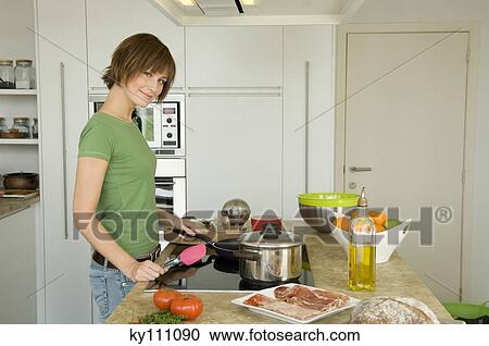 Young woman cooking, looking at the camera View Large Photo Image Stock Image - Young woman cooking, looking at the camera. Fotosearch