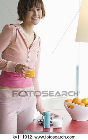Stock Image - Young woman holding glass of orange juice, smiling for the camera. Fotosearch