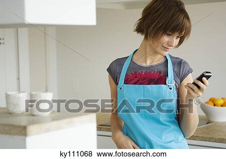 Young woman in apron, using mobile phone in kitchen View Large Photo Image Stock Photo - Young woman in apron, using mobile phone in kitchen. Fotosearch