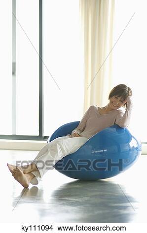 Young woman resting in blue armchair, smiling for the camera View Large Photo Image Picture - Young woman resting in blue armchair, smiling for the camera. Fotosearch