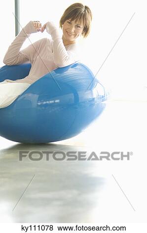 Stock Photo - Young woman resting in blue armchair, smiling for the camera. Fotosearch