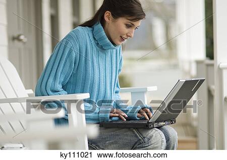 Young woman sitting on a chair, using a laptop computer, outdoors View Large Photo Image Stock Image - Young woman sitting on a chair, using a laptop computer, outdoors. Fotosearch
