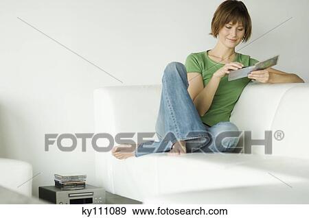 Young woman sitting on a sofa holding a CD View Large Photo Image Stock Photo - Young woman sitting on a sofa holding a CD. Fotosearch
