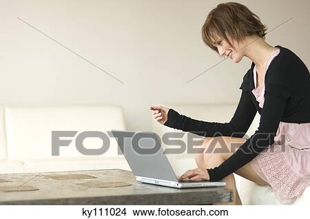 Young woman sitting on a sofa using laptop computer View Large Photo Image Picture - Young woman sitting on a sofa using laptop computer. Fotosearch