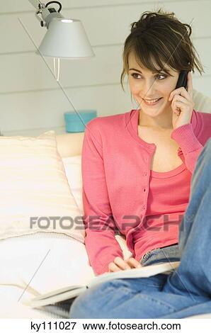 Young woman sitting on a sofa using mobile phone View Large Photo Image Stock Photo - Young woman sitting on a sofa using mobile phone. Fotosearch