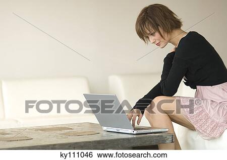 Young woman sitting on a sofa using laptop computer View Large Photo Image Stock Photograph - Young woman sitting on a sofa using laptop computer. Fotosearch