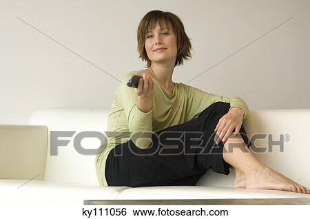 Young woman sitting on a sofa using remote-control View Large Photo Image Stock Photograph - Young woman sitting on a sofa using remote-control. Fotosearch