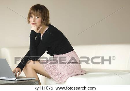 Stock Photography - Young woman sitting on a sofa using laptop computer. Fotosearch