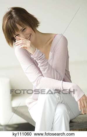 Young woman smiling, sitting on coffee table View Large Photo Image Stock Image - Young woman smiling, sitting on coffee table. Fotosearch