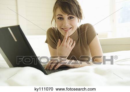 Young woman using laptop computer, lying on bed, looking at the camera View Large Photo Image Stock Image - Young woman using laptop computer, lying on bed, looking at the camera. Fotosearch