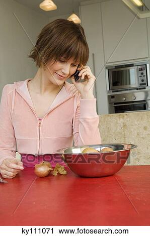 Young woman using mobile phone in kitchen, bowl of onions in front of her View Large Photo Image Stock Image - Young woman using mobile phone in kitchen, bowl of onions in front of her. Fotosearch