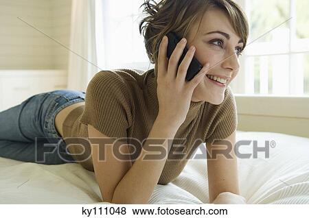 Young woman using mobile phone, lying on bed View Large Photo Image Stock Photo - Young woman using mobile phone, lying on bed. Fotosearch
