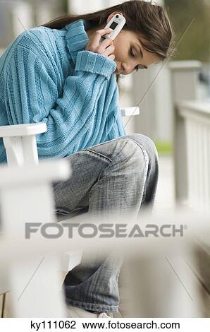 Young woman using mobile phone, sitting on a chair, outdoors View Large Photo Image Stock Image - Young woman using mobile phone, sitting on a chair, outdoors. Fotosearch