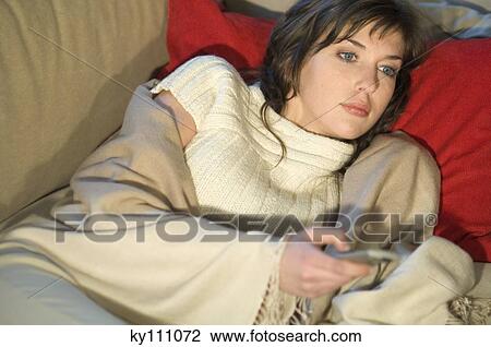 Young woman wrapped in blanket, lying on a sofa, using remote-control View Large Photo Image Stock Image - Young woman wrapped in blanket, lying on a sofa, using remote-control. Fotosearch