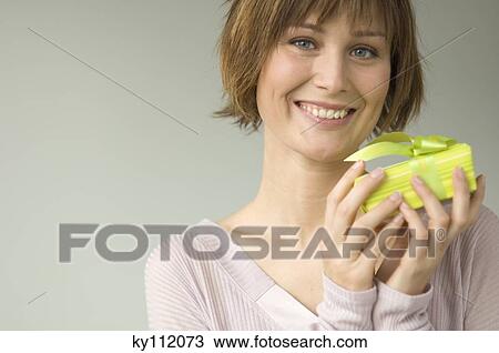 Stock Image - Portrait of a young woman holding a present, smiling for the camera. Fotosearch