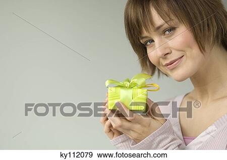 Portrait of a young woman holding a present, looking at the camera View Large Photo Image Stock Photo - Portrait of a young woman holding a present, looking at the camera. Fotosearch