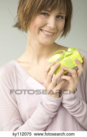 Stock Photography - Portrait of a young woman holding a present, smiling for the camera. Fotosearch