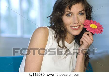 Portrait of a young woman holding plastic flower, smiling for the camera View Large Photo Image Stock Image - Portrait of a young woman holding plastic flower, smiling for the camera. Fotosearch