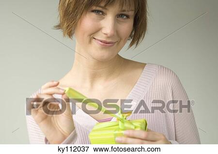 Portrait of a young woman opening a present, looking at the camera View Large Photo Image Stock Photo - Portrait of a young woman opening a present, looking at the camera. Fotosearch