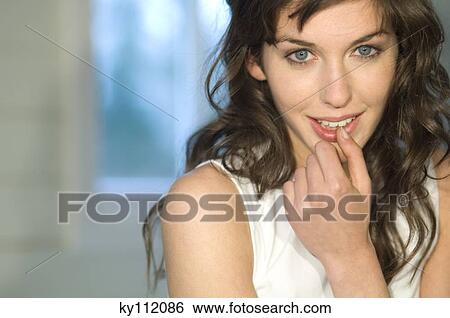 Stock Photograph - Portrait of a young woman, with finger in her mouth, looking at the camera. Fotosearch