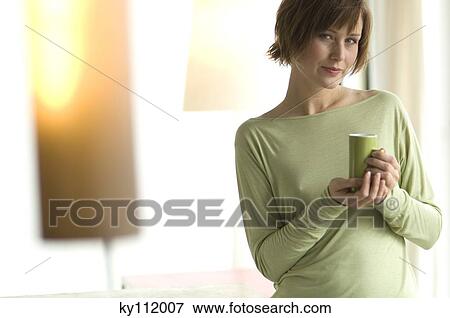 Stock Photo - Young woman holding a cup, looking at the camera. Fotosearch