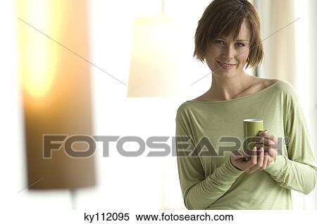 Stock Photography - Young woman holding a cup, looking at the camera. Fotosearch