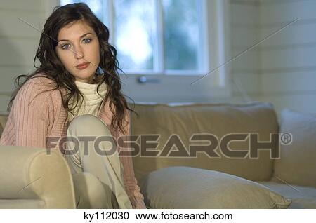 Young woman sitting on a sofa, looking at the camera View Large Photo Image Stock Image - Young woman sitting on a sofa, looking at the camera. Fotosearch